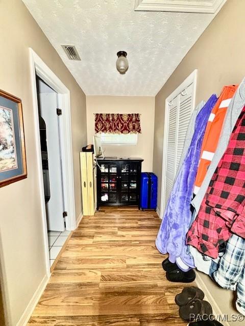 hallway featuring a textured ceiling, wood finished floors, baseboards, and visible vents