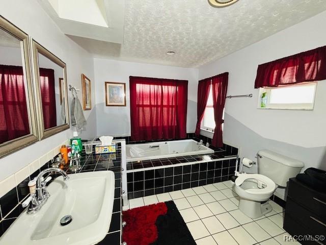 full bath featuring a garden tub, a textured ceiling, tile patterned flooring, toilet, and a sink