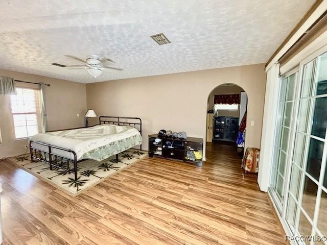 bedroom featuring a textured ceiling, a ceiling fan, visible vents, arched walkways, and wood finished floors