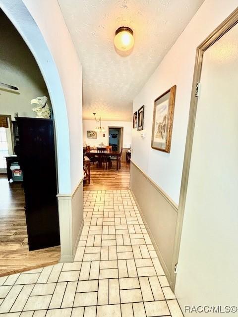 corridor featuring light wood-type flooring, arched walkways, and a textured ceiling