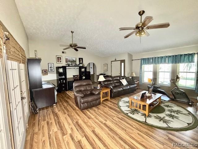 living area featuring arched walkways, ceiling fan, light wood-style floors, a textured ceiling, and lofted ceiling