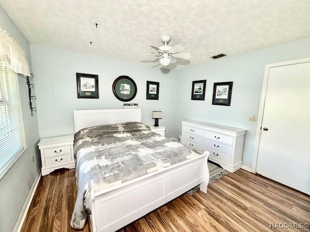 bedroom with ceiling fan, a textured ceiling, visible vents, wood finished floors, and baseboards