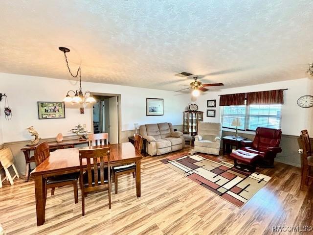 dining area featuring light wood finished floors, visible vents, a textured ceiling, and ceiling fan with notable chandelier