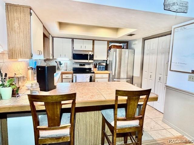 kitchen with tile counters, a tray ceiling, a peninsula, and stainless steel appliances