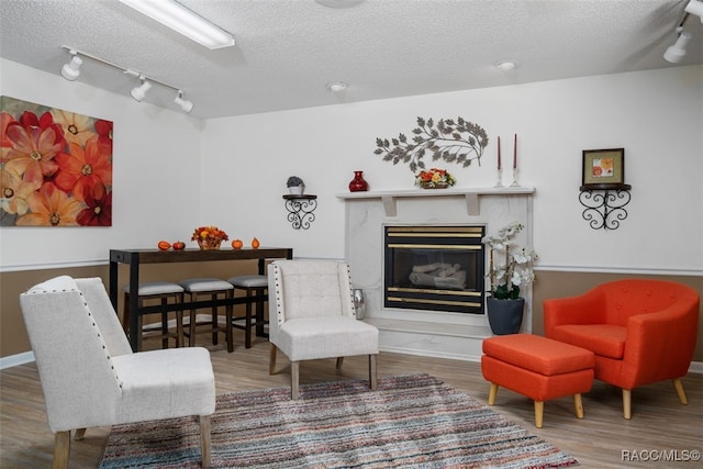 sitting room with wood-type flooring, a textured ceiling, track lighting, and a premium fireplace