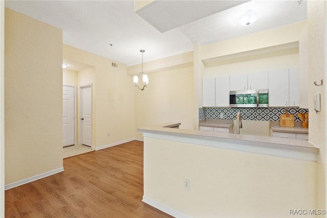 17108 Carrington Park Dr Unit 711, Tampa, FL 33647 - kitchen featuring stainless steel microwave, light wood-style flooring, white cabinets, visible vents, and hanging light fixtures