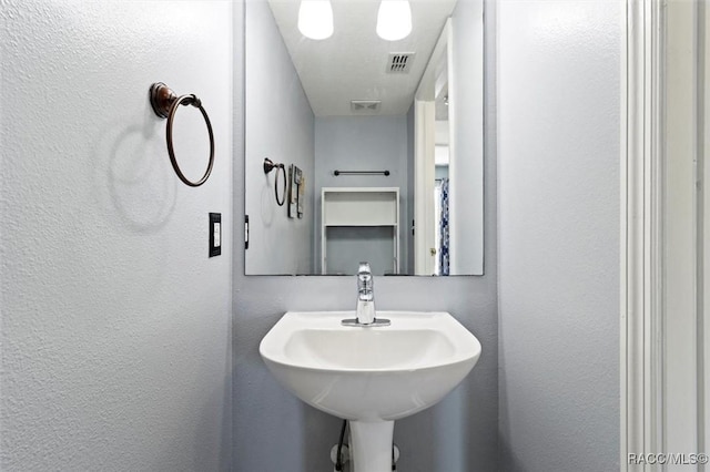 bathroom with visible vents, a textured wall, and a sink