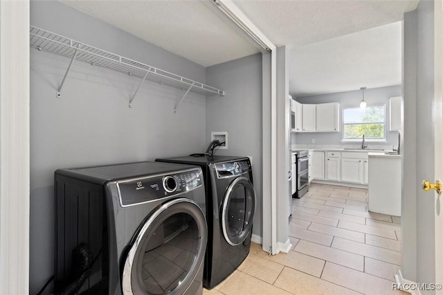washroom with light tile patterned floors, washer and clothes dryer, laundry area, and a sink