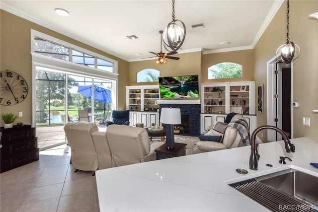 tiled living room with ceiling fan, a stone fireplace, ornamental molding, and sink