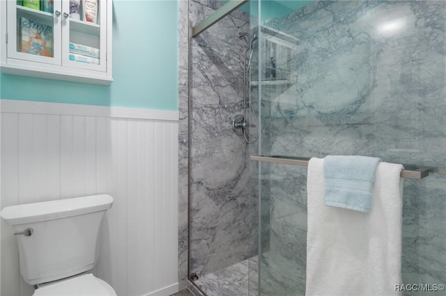 bathroom with toilet, a marble finish shower, and a wainscoted wall