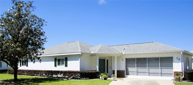 ranch-style house featuring driveway, brick siding, a garage, roof with shingles, and a front lawn