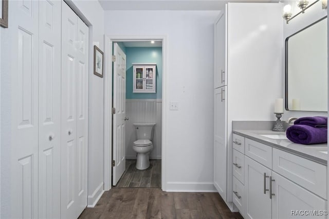 full bath featuring toilet, wood finished floors, a wainscoted wall, a closet, and vanity