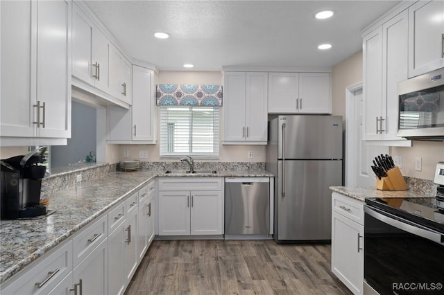 kitchen with light wood finished floors, a sink, white cabinets, light stone countertops, and appliances with stainless steel finishes