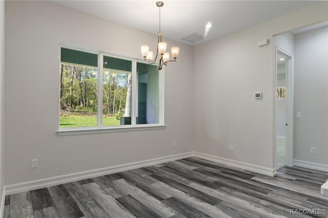 spare room featuring a chandelier, wood finished floors, and baseboards