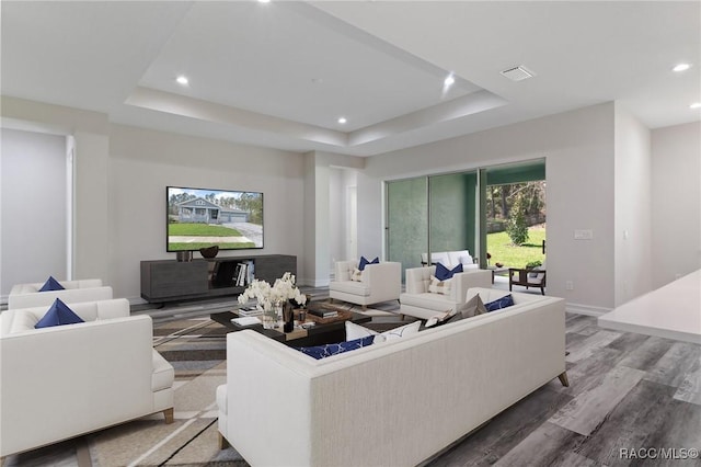 living area with baseboards, wood finished floors, recessed lighting, and a tray ceiling