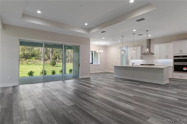 unfurnished living room with a tray ceiling, a wealth of natural light, dark wood-type flooring, and visible vents