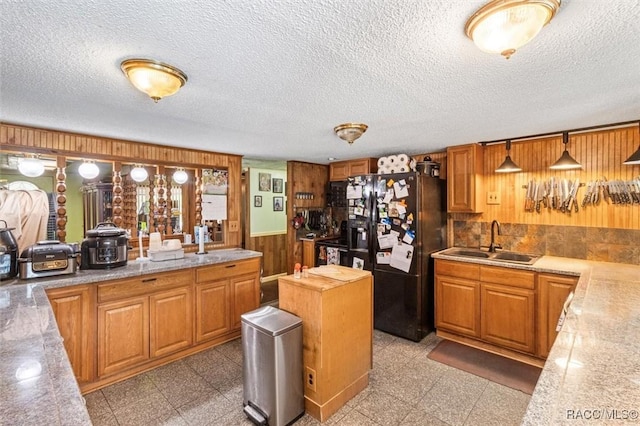 kitchen featuring a sink, wainscoting, black fridge with ice dispenser, granite finish floor, and wooden walls
