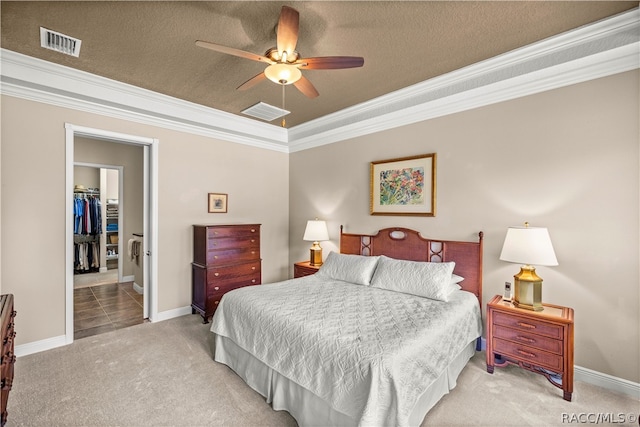 carpeted bedroom featuring crown molding, ceiling fan, a spacious closet, a textured ceiling, and a closet