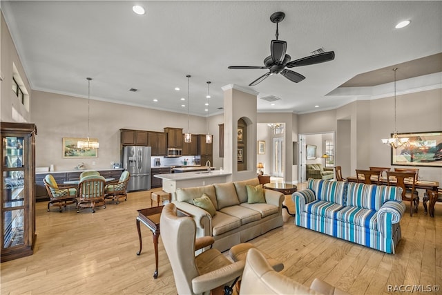 living room featuring ceiling fan with notable chandelier, light hardwood / wood-style floors, crown molding, and sink