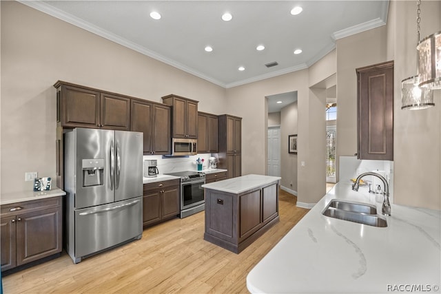 kitchen featuring sink, light wood-type flooring, ornamental molding, appliances with stainless steel finishes, and a kitchen island