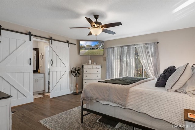 bedroom with ceiling fan, a barn door, dark hardwood / wood-style flooring, and ensuite bath