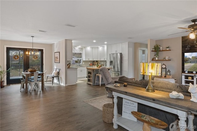 living room with ceiling fan with notable chandelier and dark hardwood / wood-style floors