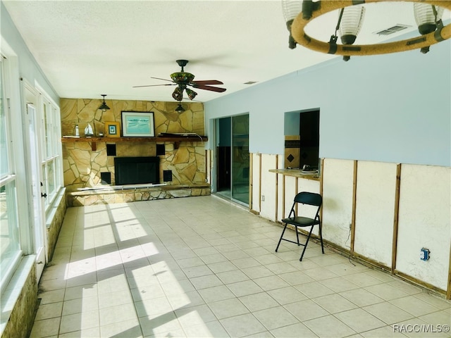 unfurnished living room with ceiling fan, a stone fireplace, and light tile patterned floors