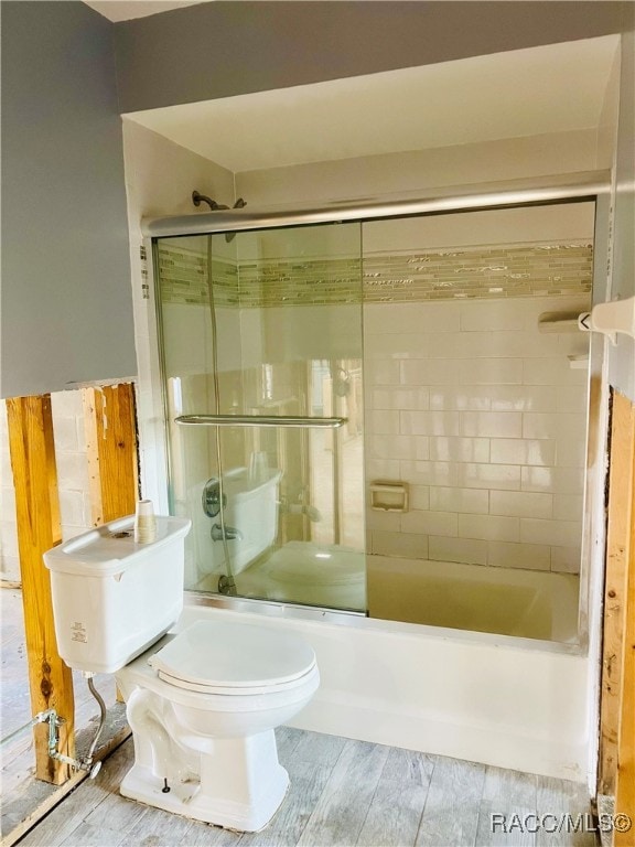 bathroom with wood-type flooring, toilet, and bath / shower combo with glass door