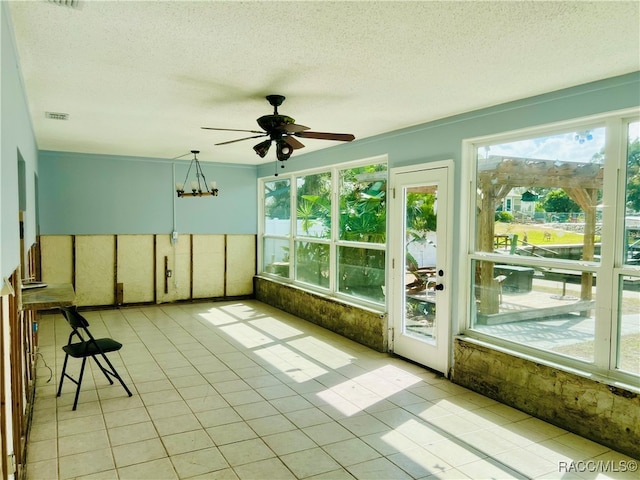 unfurnished sunroom featuring ceiling fan with notable chandelier and a healthy amount of sunlight