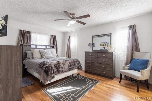 bedroom featuring ceiling fan, multiple windows, a textured ceiling, and light hardwood / wood-style flooring