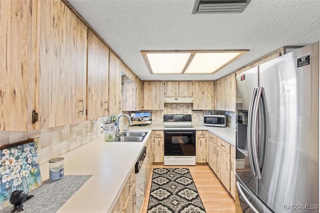 kitchen with a textured ceiling, stainless steel appliances, light brown cabinetry, and sink