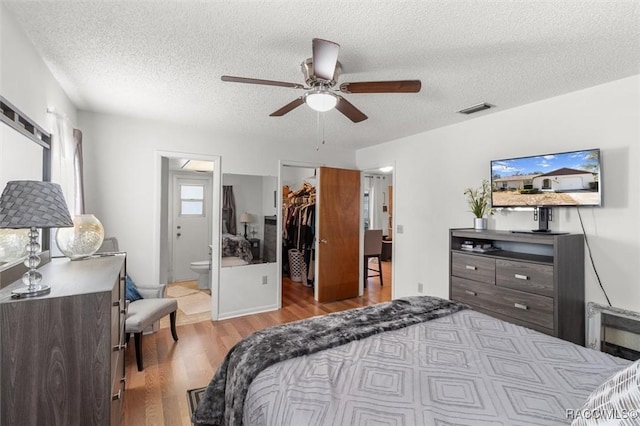 bedroom featuring ensuite bathroom, ceiling fan, a textured ceiling, a walk in closet, and light hardwood / wood-style flooring