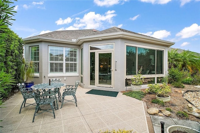 back of house with roof with shingles, outdoor dining space, stucco siding, and a patio area