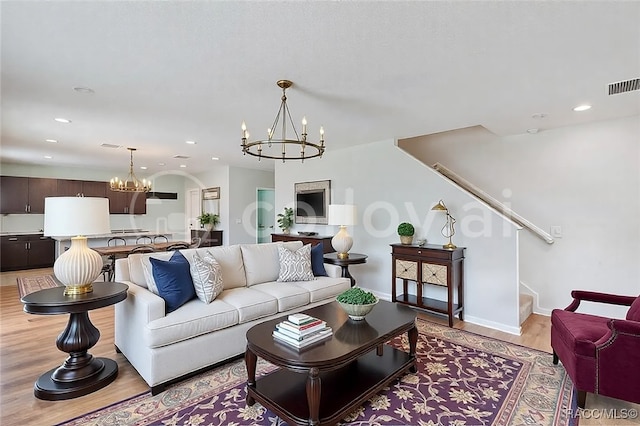 living room featuring light wood finished floors, baseboards, visible vents, stairway, and an inviting chandelier