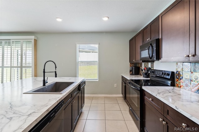 kitchen with light stone counters, dark brown cabinetry, sink, black appliances, and light tile patterned floors