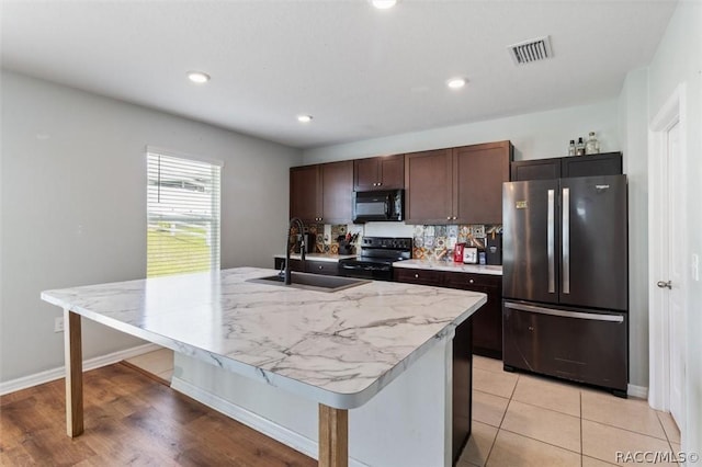 kitchen featuring visible vents, light countertops, a sink, an island with sink, and black appliances