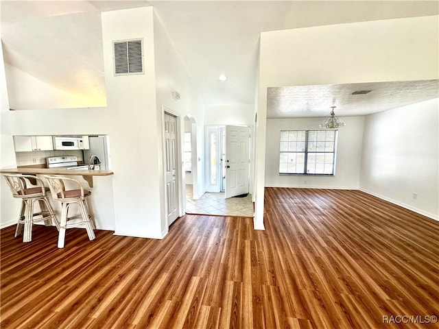 unfurnished living room with hardwood / wood-style floors, a high ceiling, a textured ceiling, and a notable chandelier