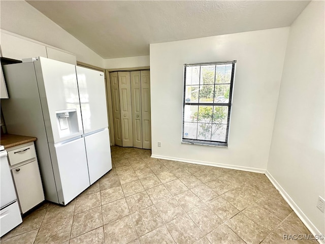 kitchen with a textured ceiling, white appliances, vaulted ceiling, light tile patterned floors, and white cabinets