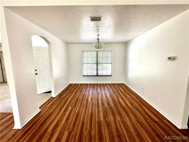 unfurnished room with a textured ceiling, dark wood-type flooring, and a notable chandelier