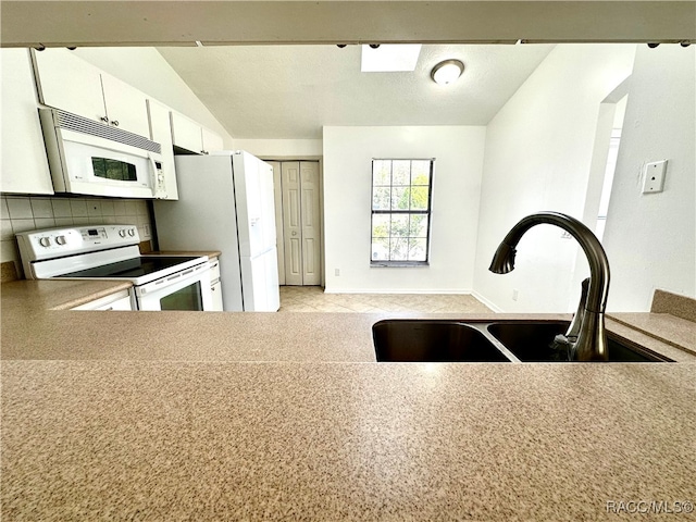 kitchen with tasteful backsplash, white appliances, vaulted ceiling, sink, and white cabinets