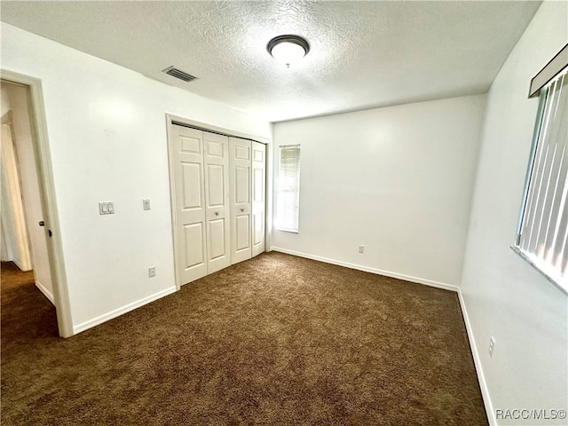 unfurnished bedroom featuring dark colored carpet, a textured ceiling, and a closet