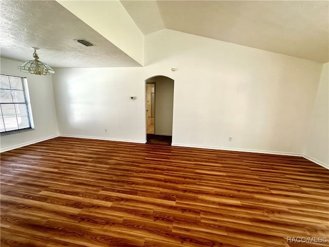 spare room with a textured ceiling, dark wood-type flooring, and vaulted ceiling