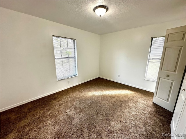 spare room featuring a textured ceiling and dark carpet