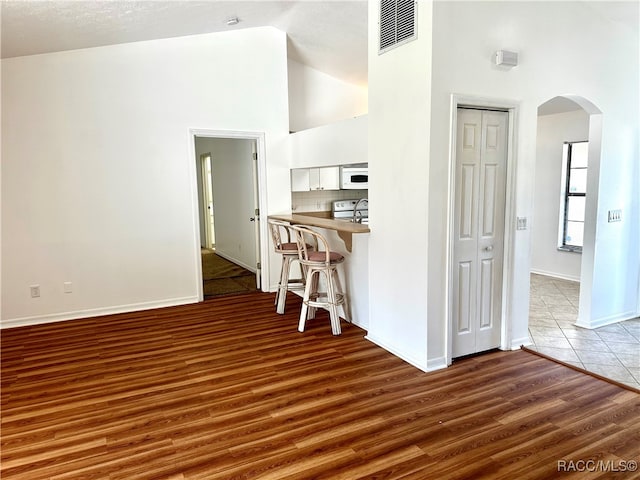 kitchen featuring white appliances, high vaulted ceiling, white cabinets, dark hardwood / wood-style floors, and a kitchen bar