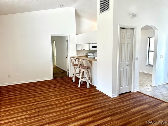 3150 W Mustang Blvd, Beverly Hills, FL 34465 - kitchen featuring arched walkways, a breakfast bar, high vaulted ceiling, wood finished floors, and white cabinetry