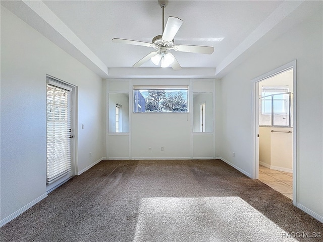 unfurnished room featuring a tray ceiling, a wealth of natural light, ceiling fan, and carpet flooring