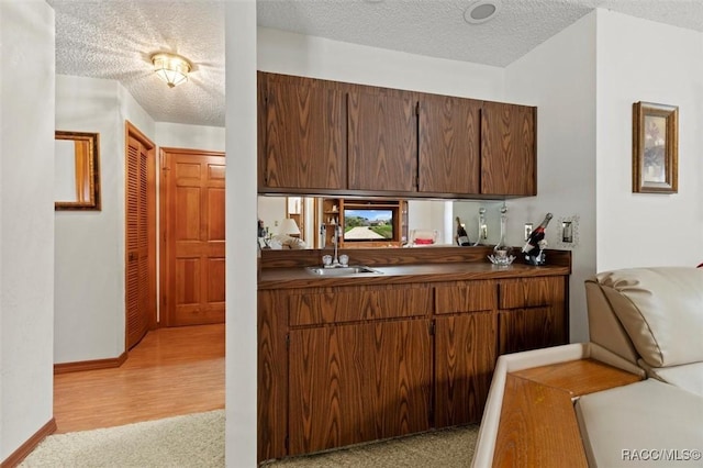 kitchen with a textured ceiling, dark countertops, baseboards, and a sink