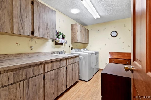 clothes washing area featuring light wood-style flooring, cabinet space, a sink, a textured ceiling, and washing machine and dryer