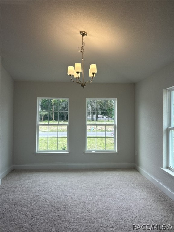 empty room featuring carpet, a healthy amount of sunlight, and an inviting chandelier