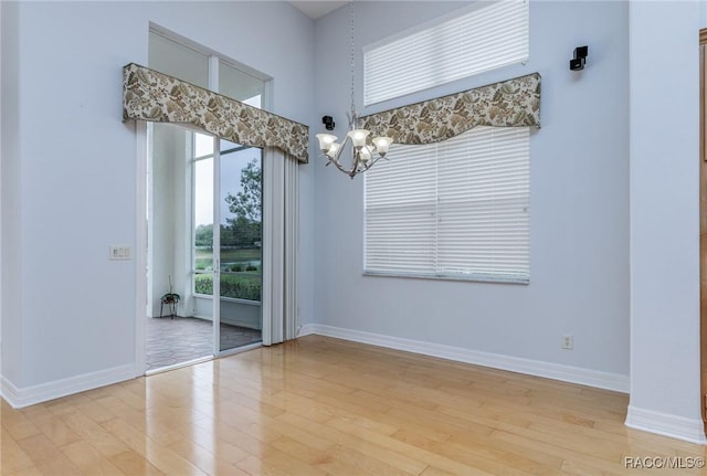 spare room featuring light wood-style floors, a high ceiling, baseboards, and an inviting chandelier